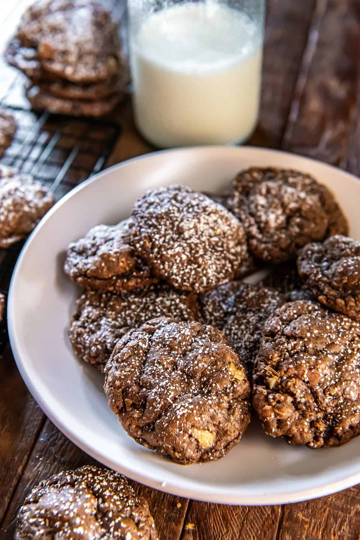 Chocolate Oatmeal Cookies 3 Chocolate oatmeal cookies dusted with powdered sugar on a white plate in front of a glass of milk.