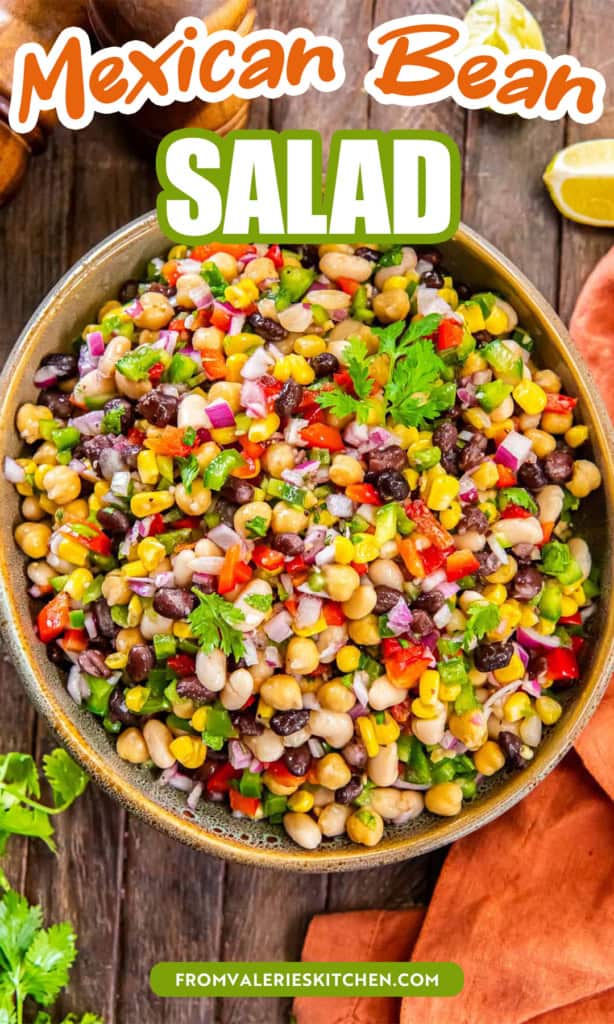 Mexican bean salad with three types of beans, corn, and bell peppers in a large wood bowl next to an orange kitchen cloth with overlay text.