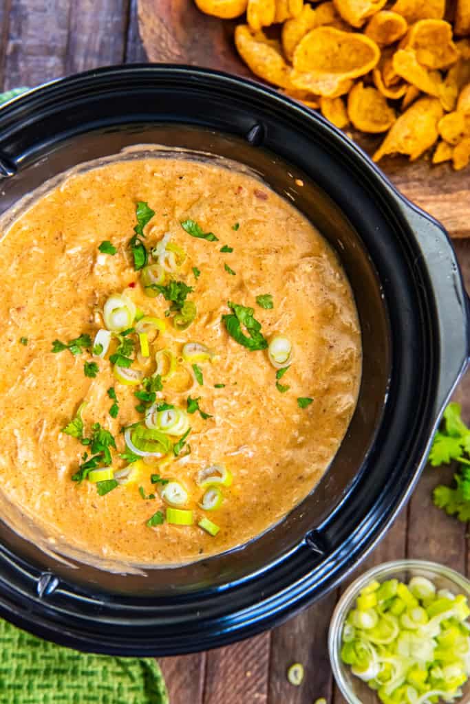 Chicken enchilada dip in a slow cooker topped with sliced green onions and cilantro.