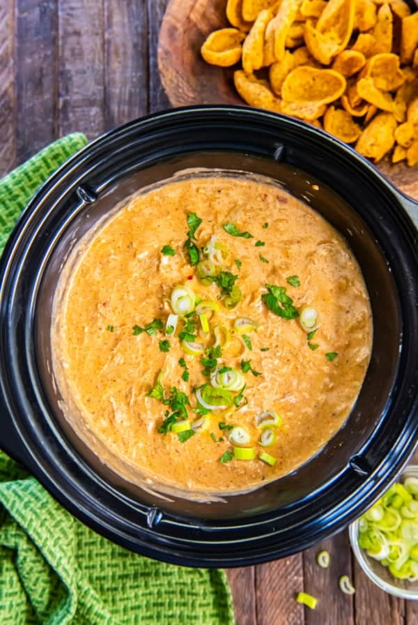 Chicken enchilada dip in a slow cooker topped with sliced green onions and cilantro.