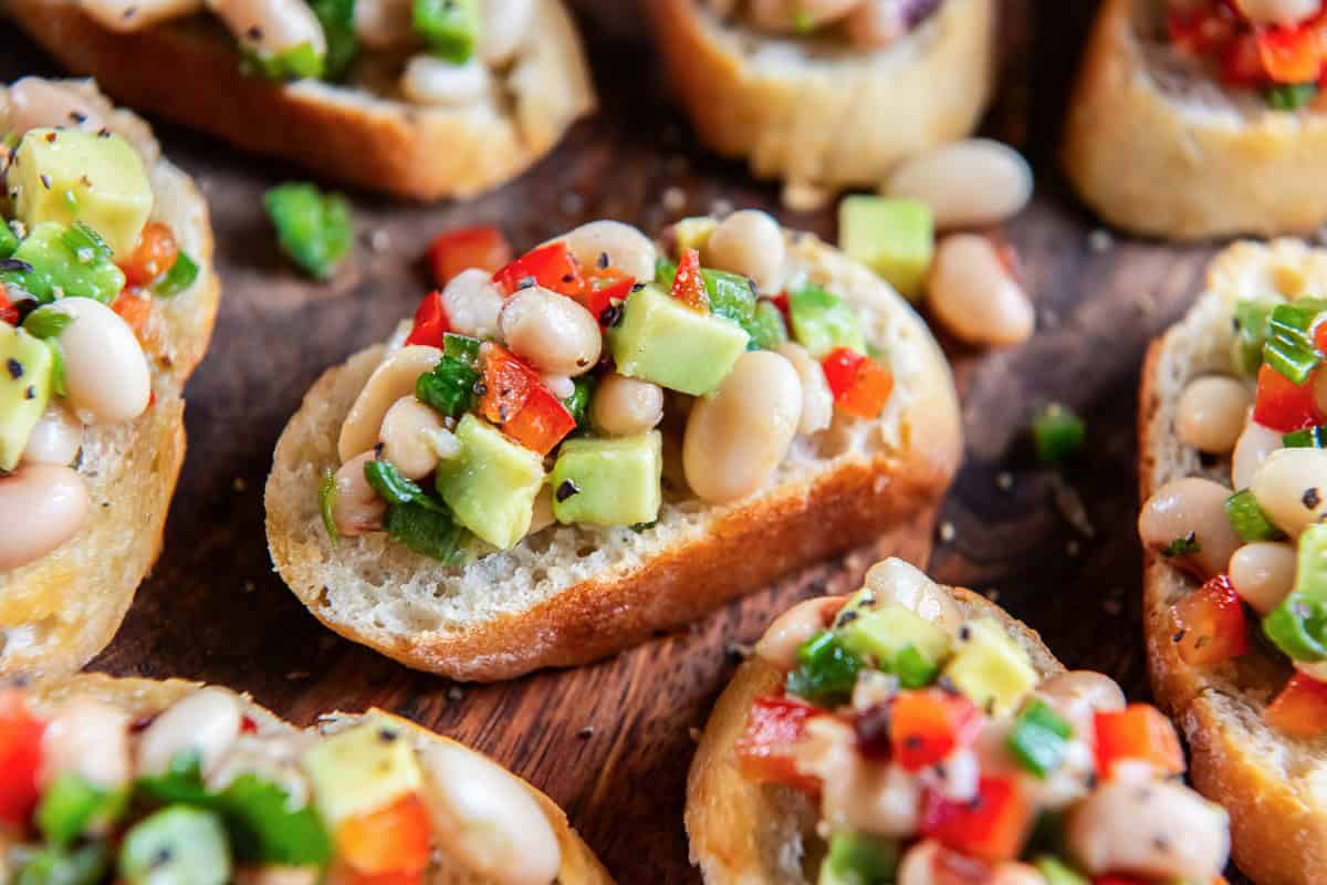 White bean crostini with black eyed peas and avocado on a wood platter.