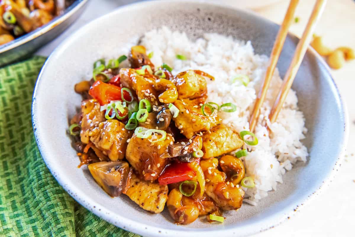 Chopsticks resting in a bowl with cashew chicken and white rice.
