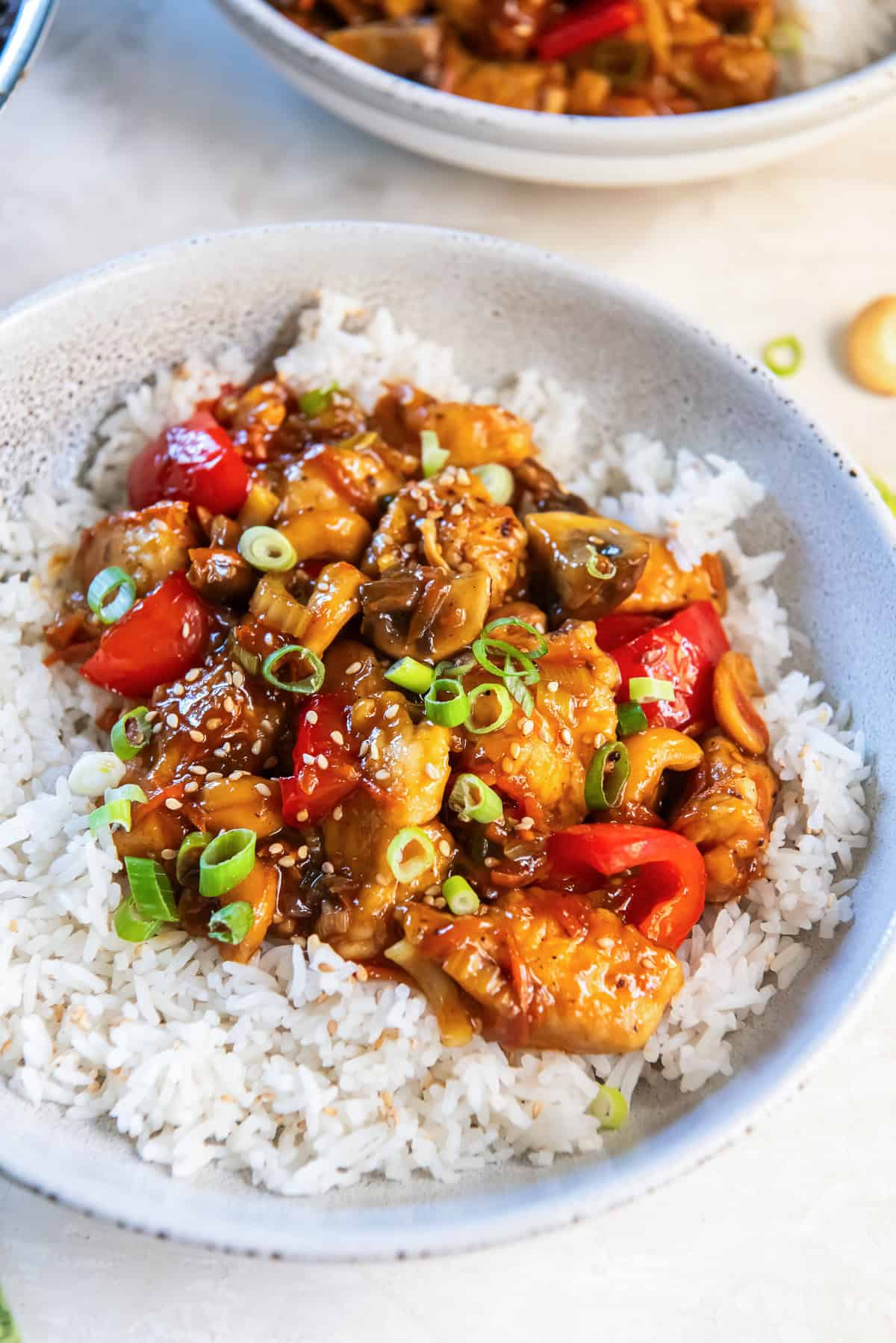 Cashew chicken with red bell pepper and mushrooms in a white bowl with white rice.