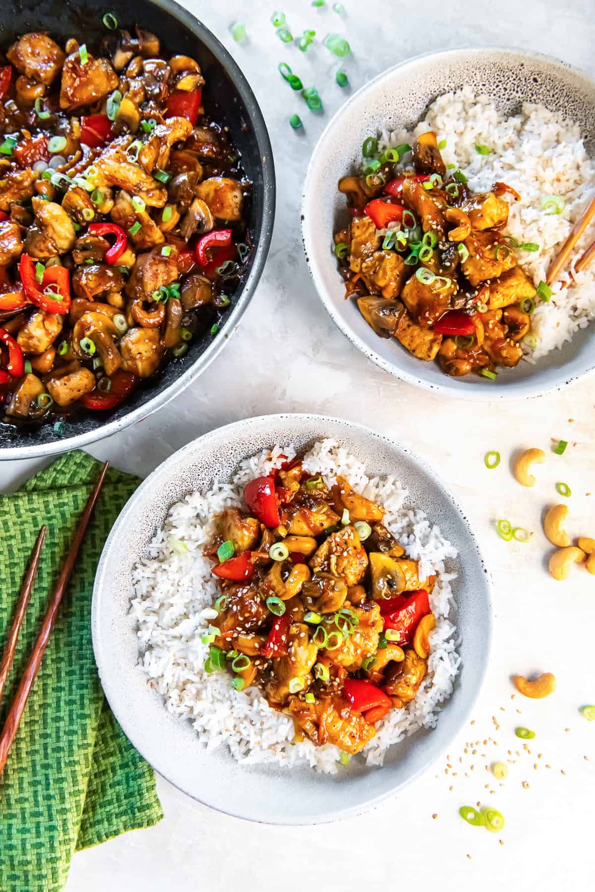Two bowls of cashew chicken and rice next to a skillet full.