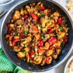 Cashew chicken with bell peppers, carrots, and mushrooms in a skillet.