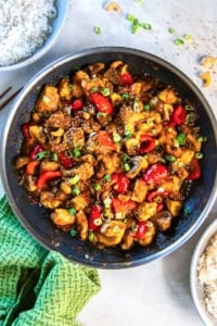 Cashew chicken with bell peppers, carrots, and mushrooms in a skillet.