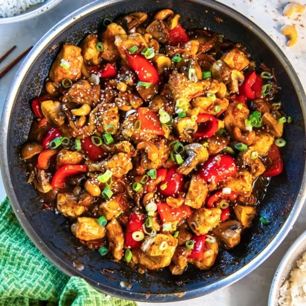 Cashew chicken with bell peppers, carrots, and mushrooms in a skillet.