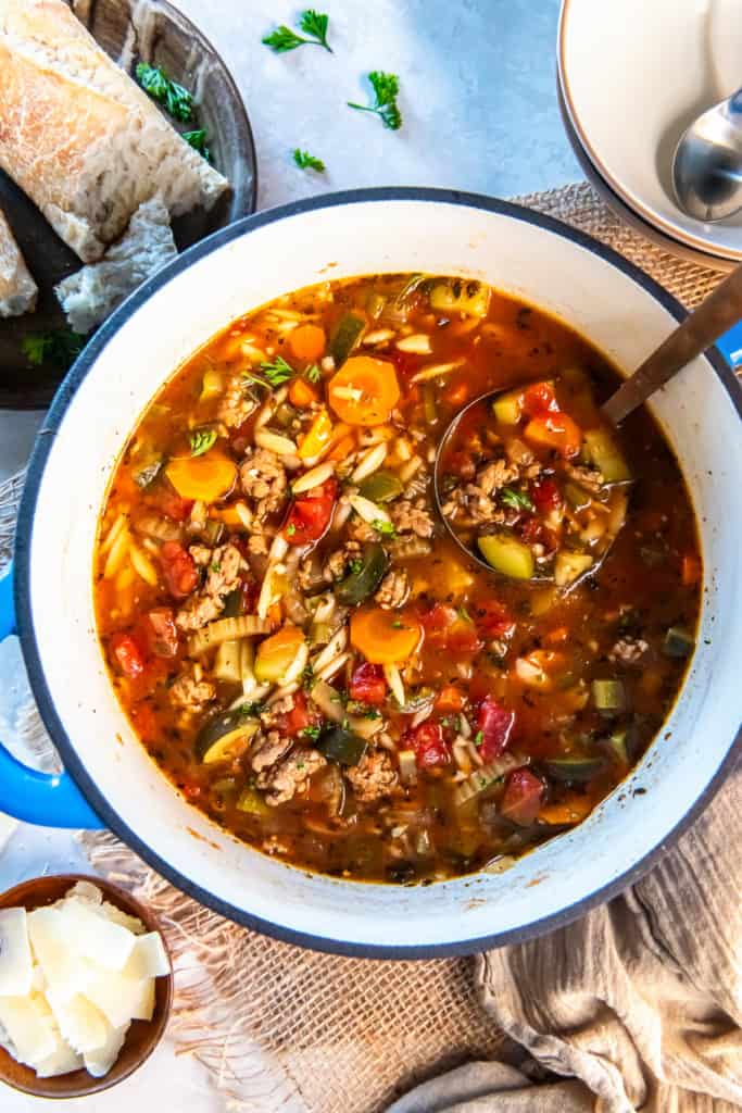 A ladle resting in a Dutch oven filled with Italian sausage zucchini soup.