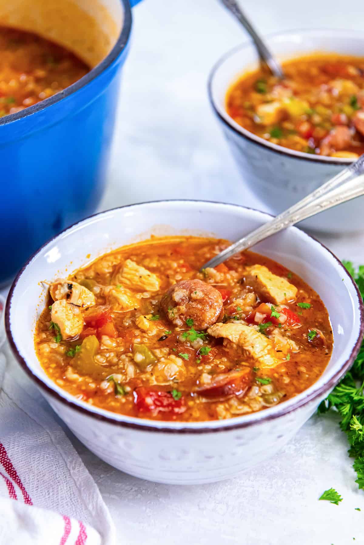 A bowl of Jambalaya Soup showing sliced sausage, chicken, and vegetables with parsley garnish