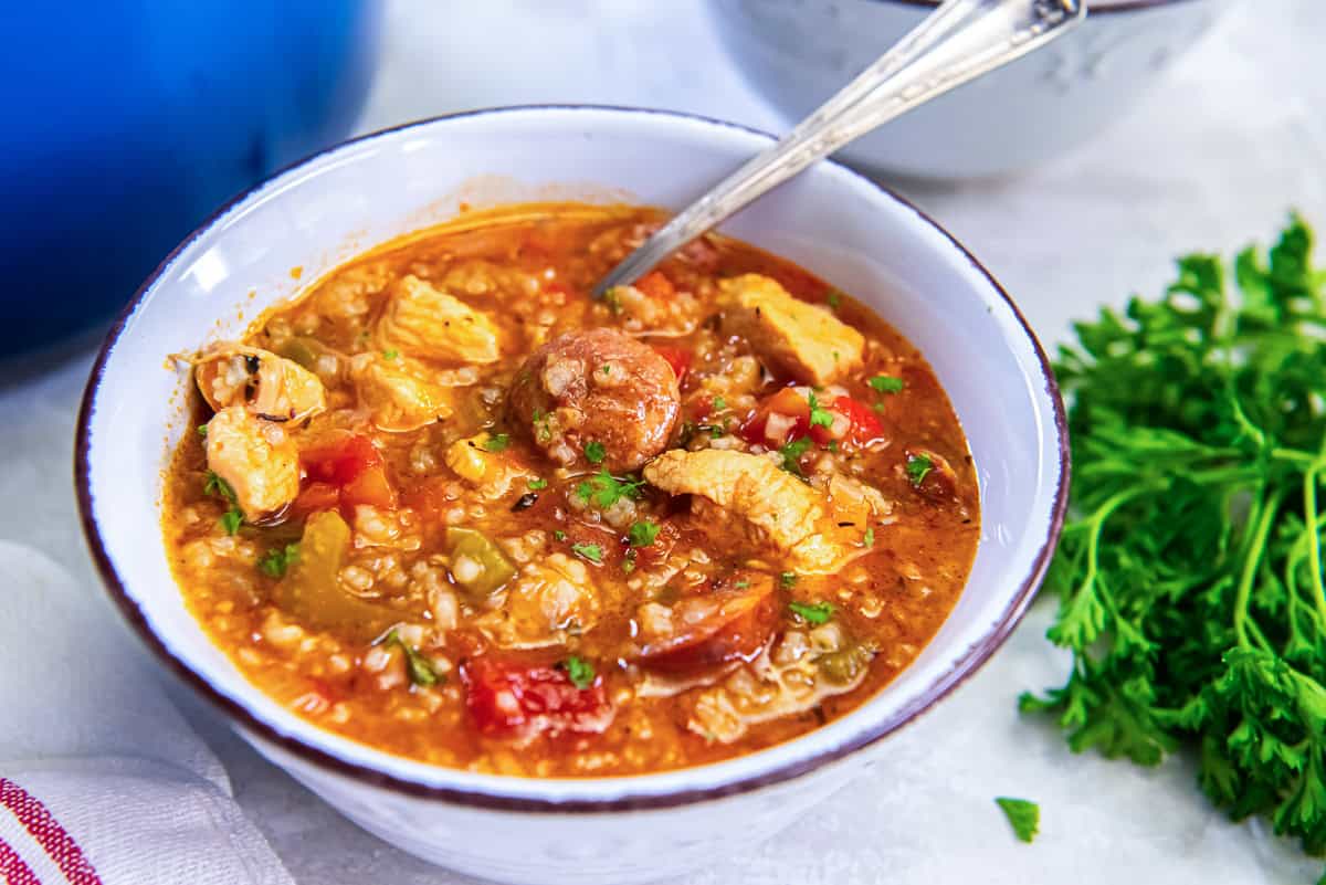 A bowl of Jambalaya Soup showing sliced sausage, chicken, and vegetables with parsley garnish