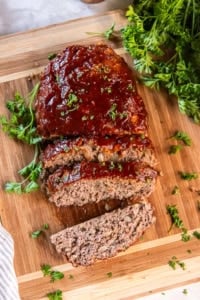 A small sliced meatloaf with glaze on a cutting board.