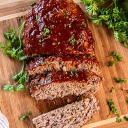 A small sliced meatloaf with glaze on a cutting board.
