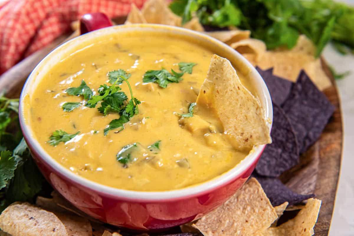 Slow cooker chicken queso dip in a small bowl on a platter with tortilla chips.