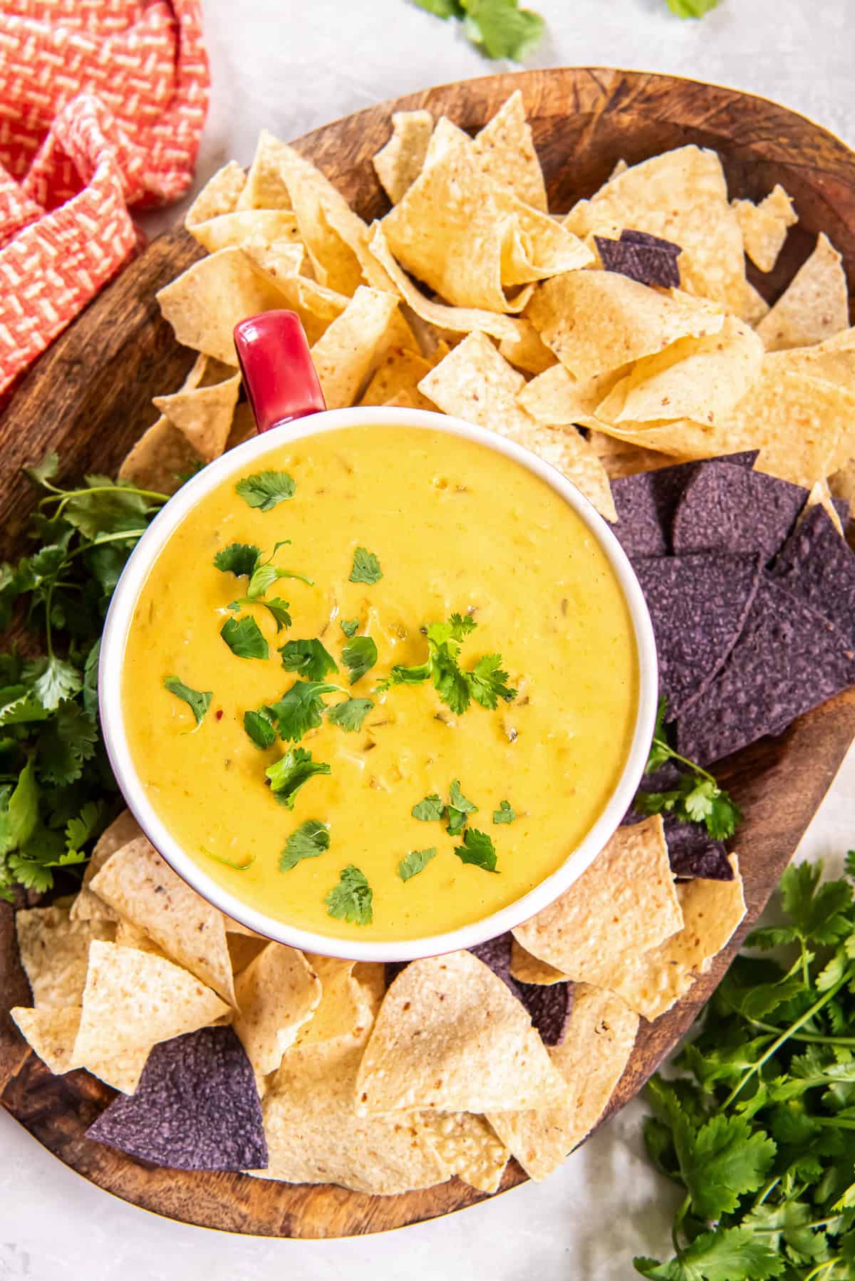 Chicken queso dip in a red-handled bowl on a wood board with blue and white corn chips.