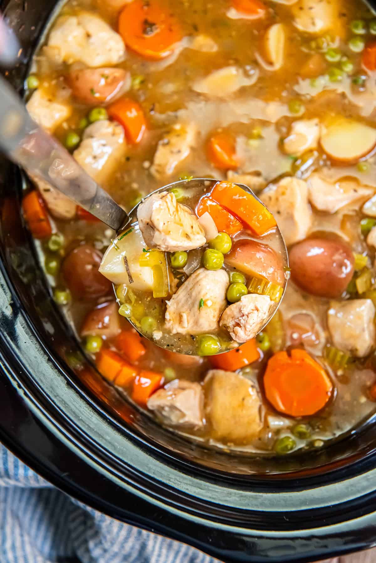 A ladle scooping chicken stew from a slow cooker.