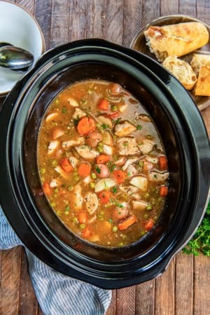 Chicken stew in a slow cooker with carrots, potatoes, peas, and tender chicken.