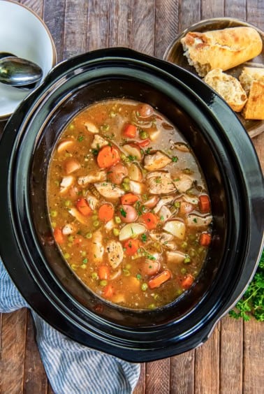 Chicken stew in a slow cooker with carrots, potatoes, peas, and tender chicken.
