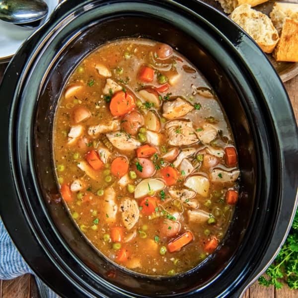 Chicken stew in a slow cooker with carrots, potatoes, peas, and tender chicken.