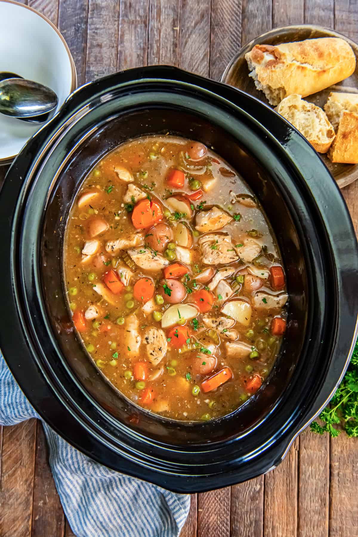 Chicken stew in a slow cooker with carrots, potatoes, peas, and tender chicken.