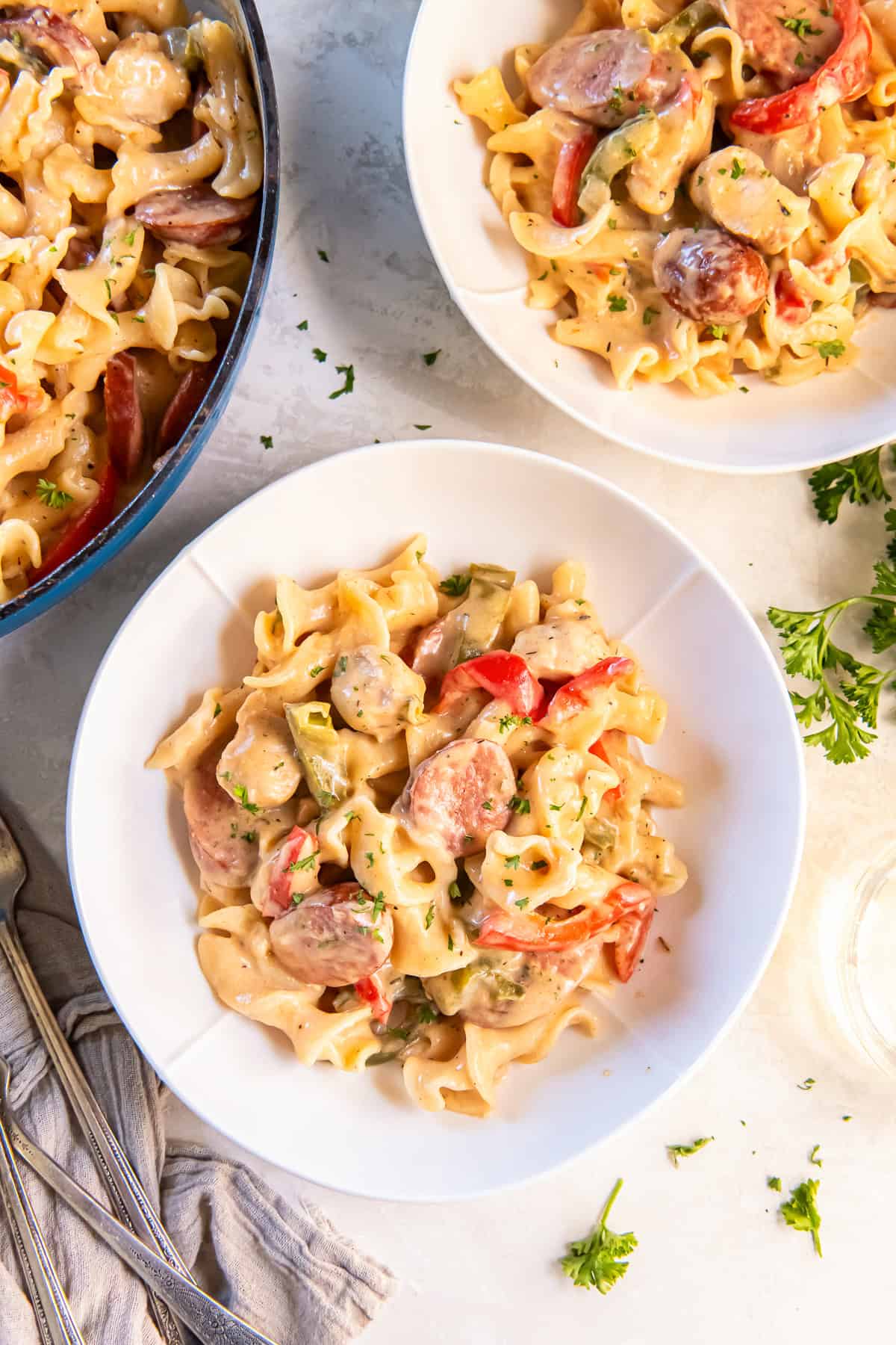 Bowls of creamy Cajun Chicken and Sausage Pasta served on a light surface with colorful bell peppers and parsley.