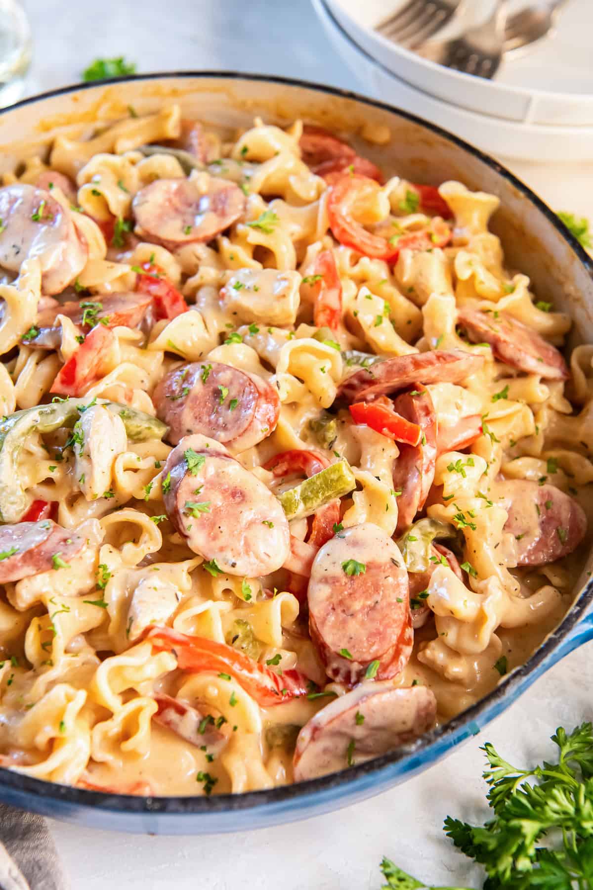 creamy Cajun Chicken and Sausage Pasta in a blue pan with slices of sausage, bell peppers, and herbs.