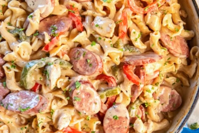 Creamy Cajun Chicken and Sausage Pasta in a blue Dutch oven with colorful bell peppers and fresh parsley.