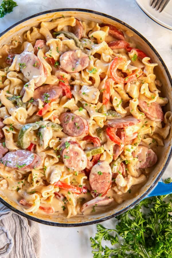 Creamy Cajun Chicken and Sausage Pasta in a blue Dutch oven with colorful bell peppers and fresh parsley.
