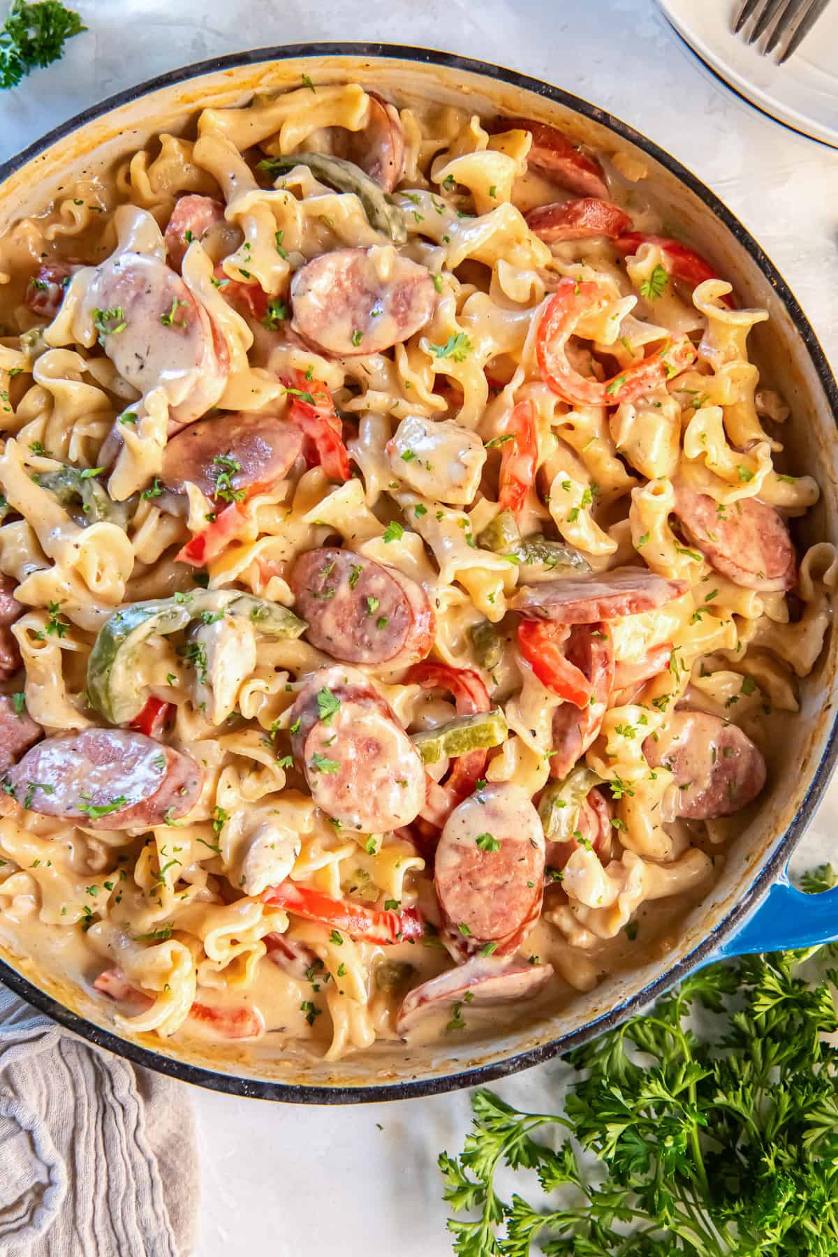 Creamy Cajun Chicken and Sausage Pasta in a blue Dutch oven with colorful bell peppers and fresh parsley.