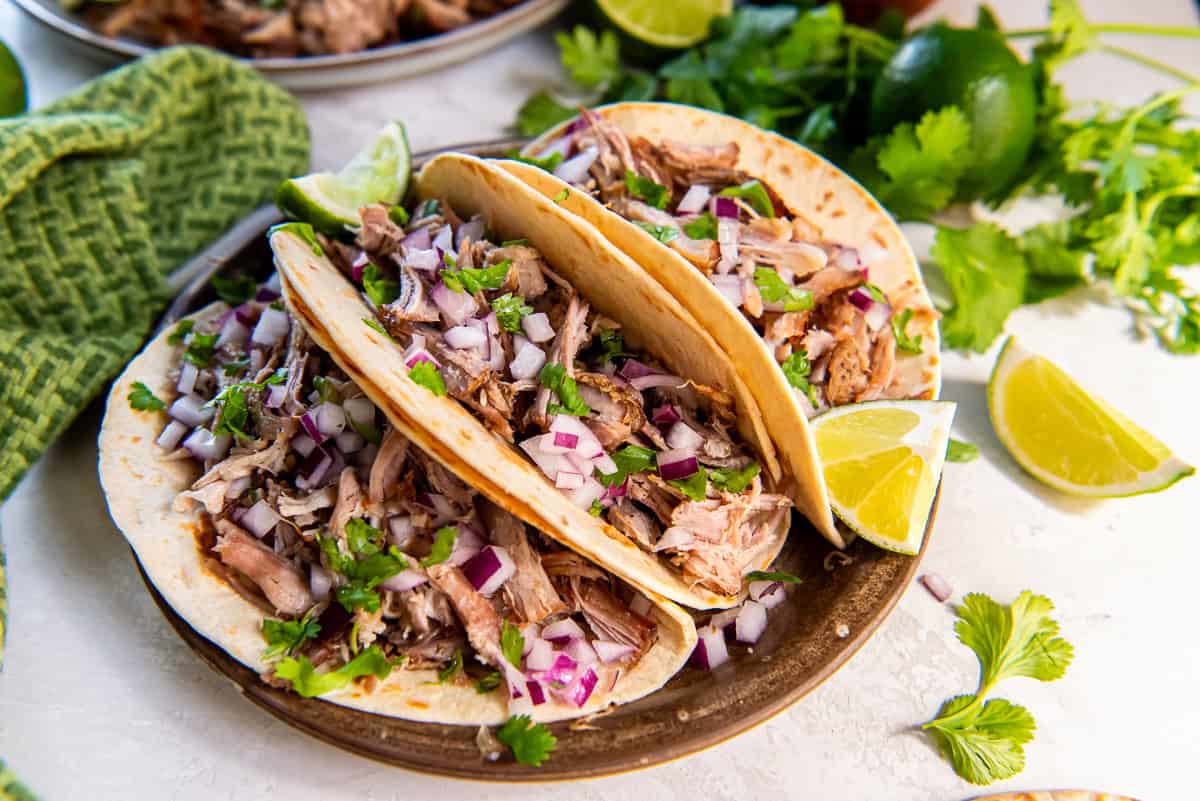 Carnitas tacos topped with red onion, cilantro, and lime.