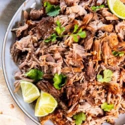 Crispy shredded pork carnitas on a platter with lime wedges and cilantro.