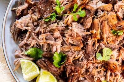 Crispy shredded pork carnitas on a platter with lime wedges and cilantro.