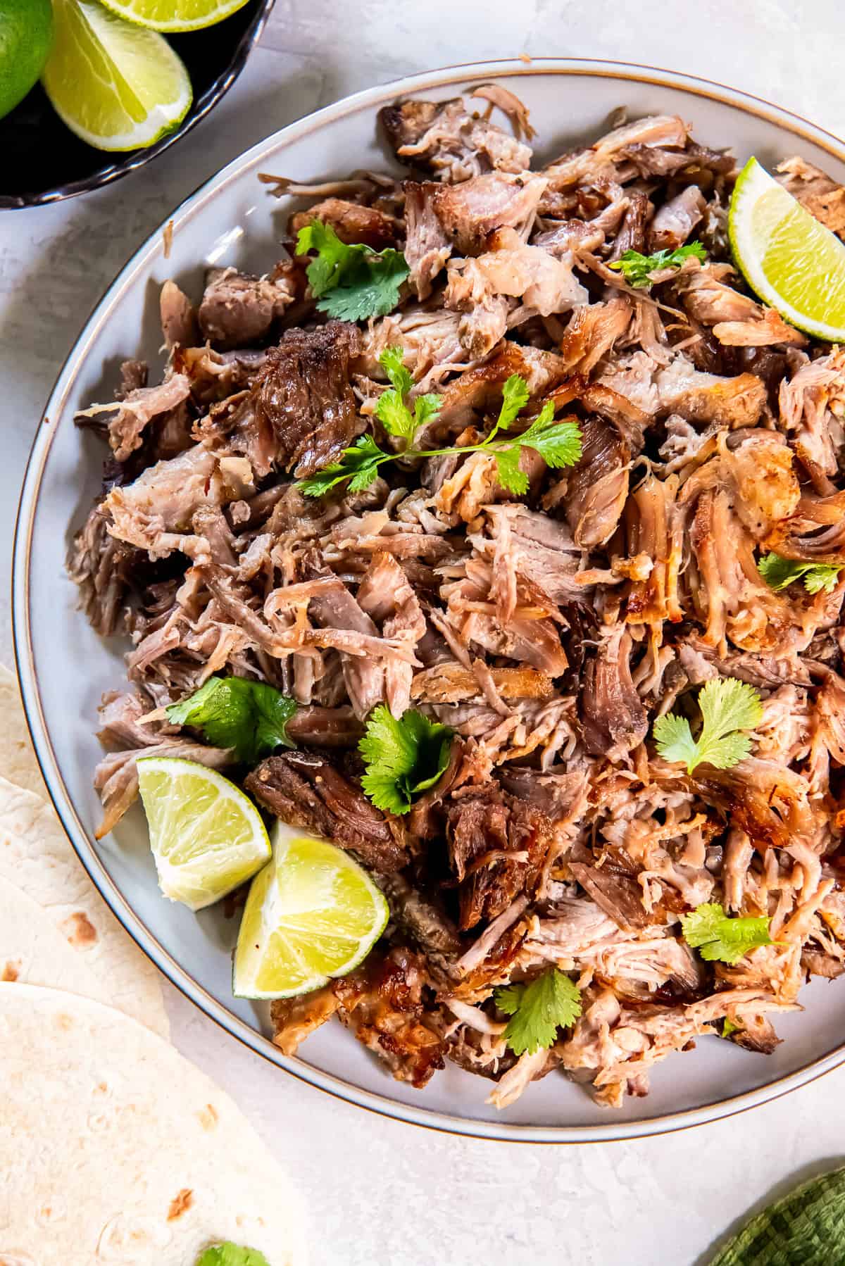 Crispy shredded pork carnitas on a platter with lime wedges and cilantro.
