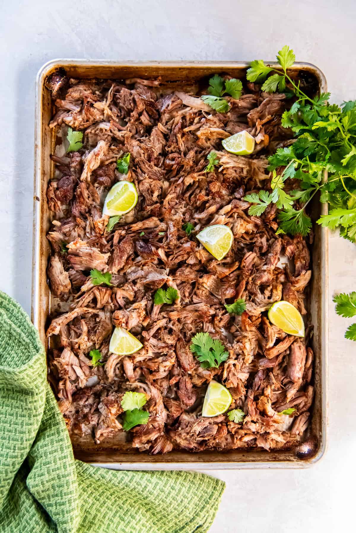 Crisped pork carnitas on a baking sheet with lime wedges and cilantro.