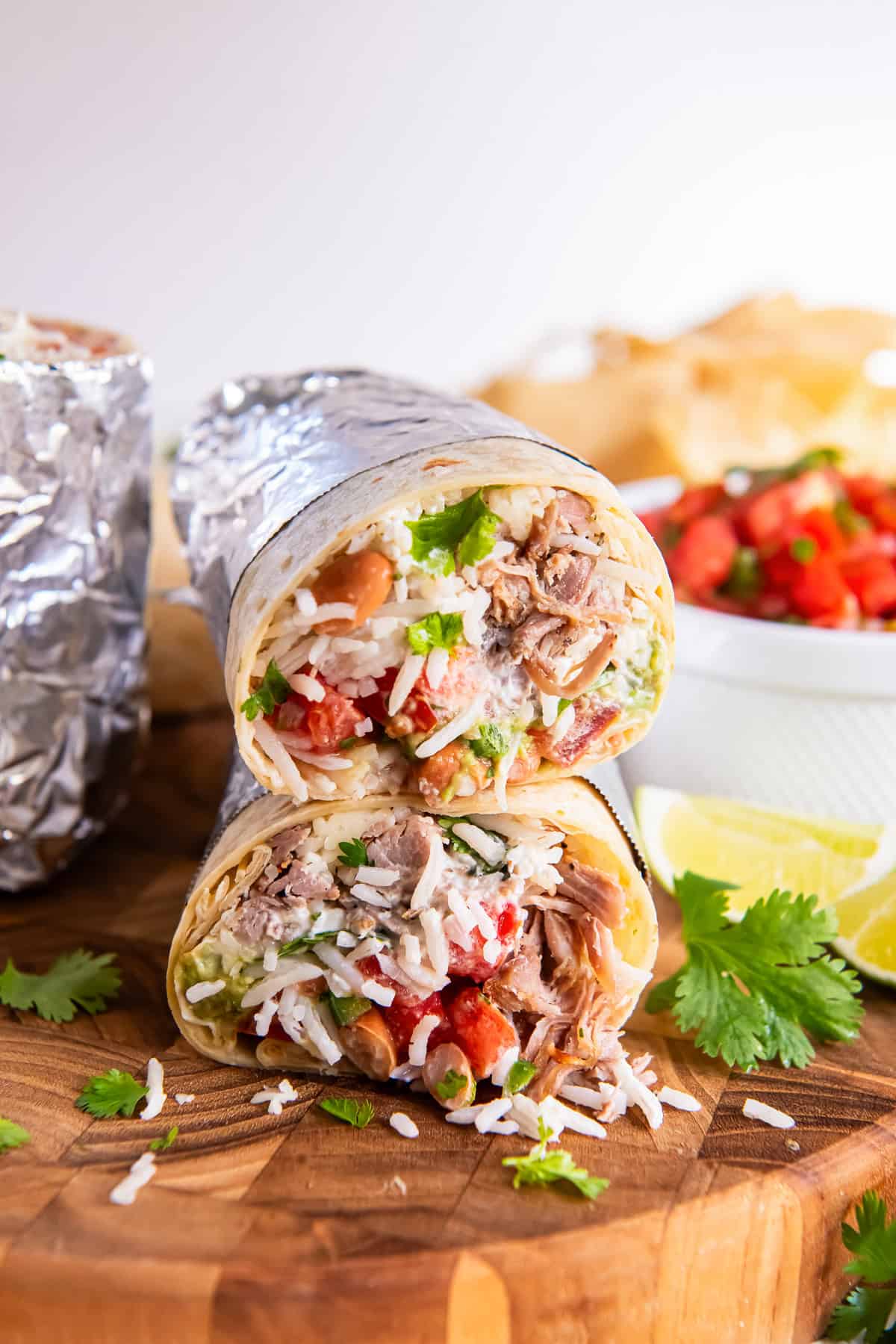 A foil wrapped carnitas burrito sliced in half and stacked on a wooden board.