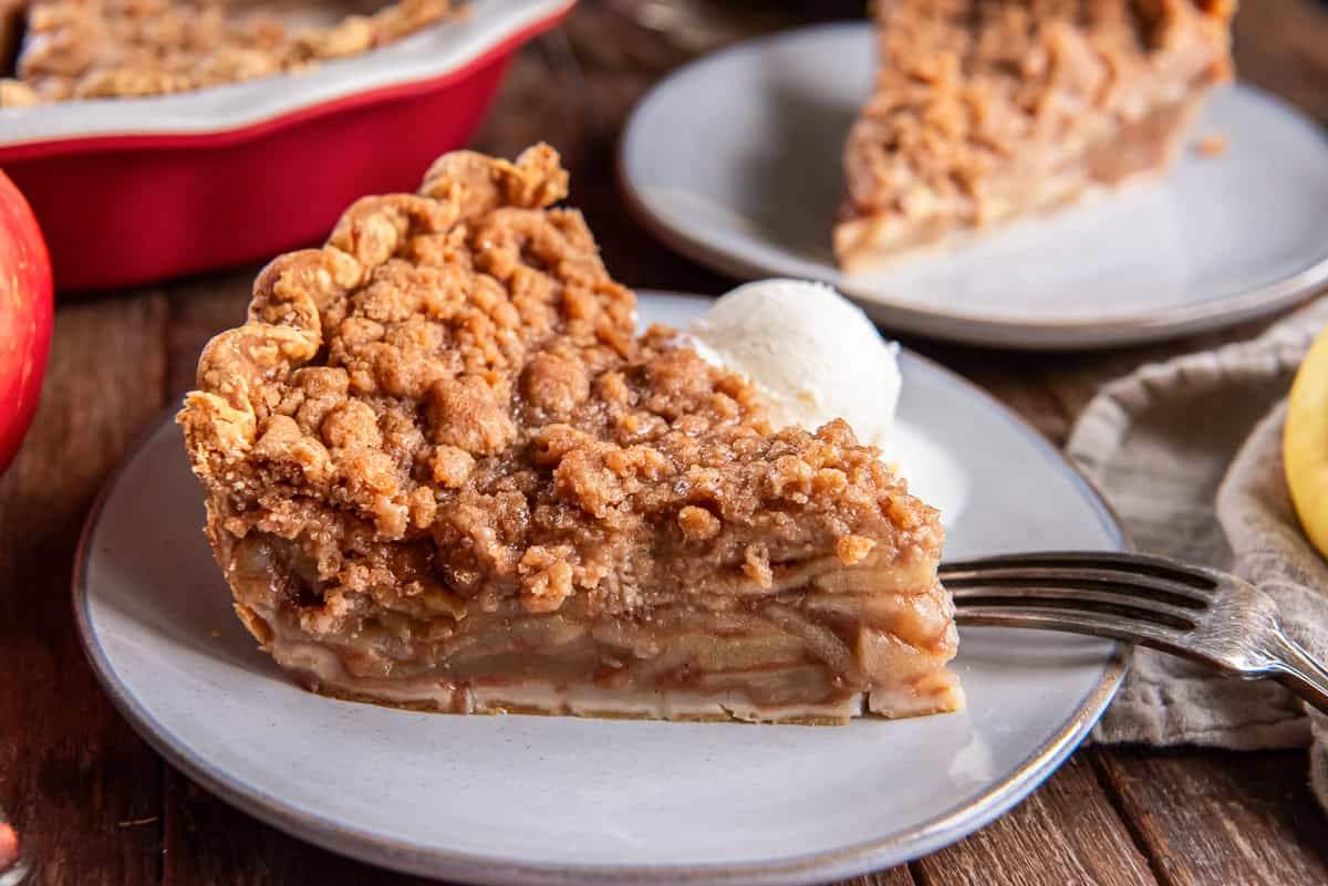 A slice of Dutch apple pie with a crumb topping served on a plate with a scoop of vanilla ice cream.