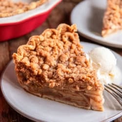 A slice of Dutch apple pie with a crumb topping served on a plate with a scoop of vanilla ice cream, with the remaining pie in the background.