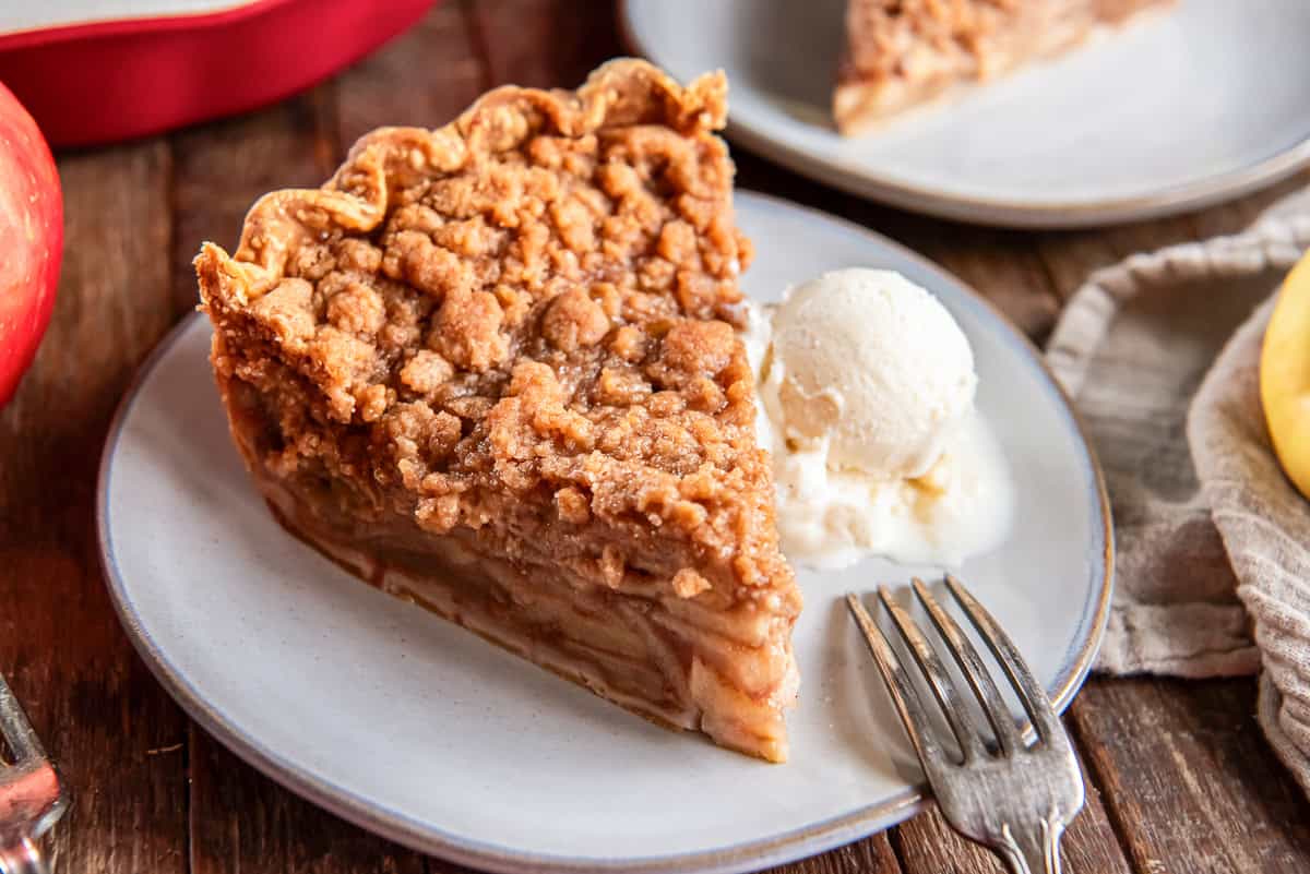 A slice of Dutch apple pie on a white plate with ice cream.