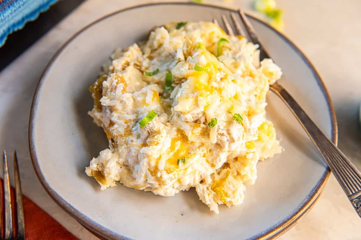 Serving of creamy green chile rice casserole with melted cheese and green onions on a plate with a fork.