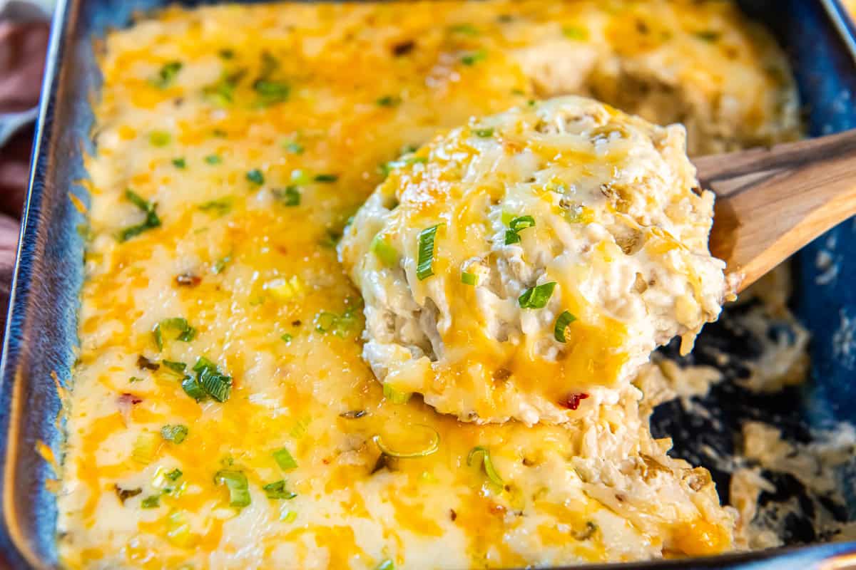 Cheesy green chile rice casserole side dish with sour cream and Monterey Jack, topped with melted cheese and green onions, with a scoop lifted from the baking dish.