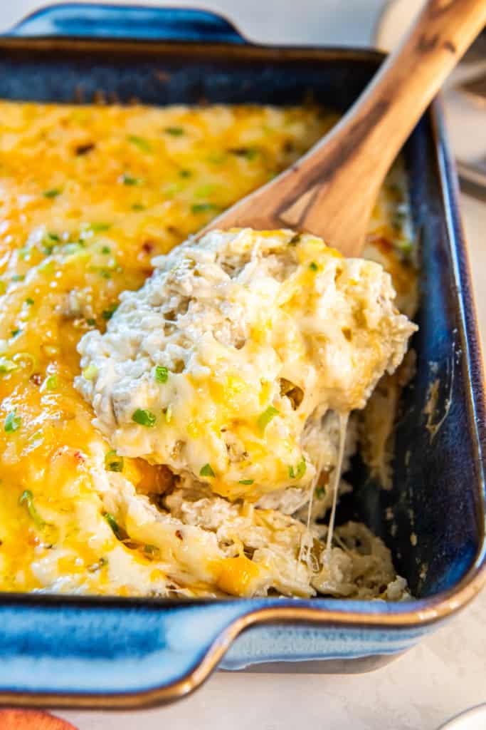 A wooden spoon scooping green chile rice from a casserole dish.