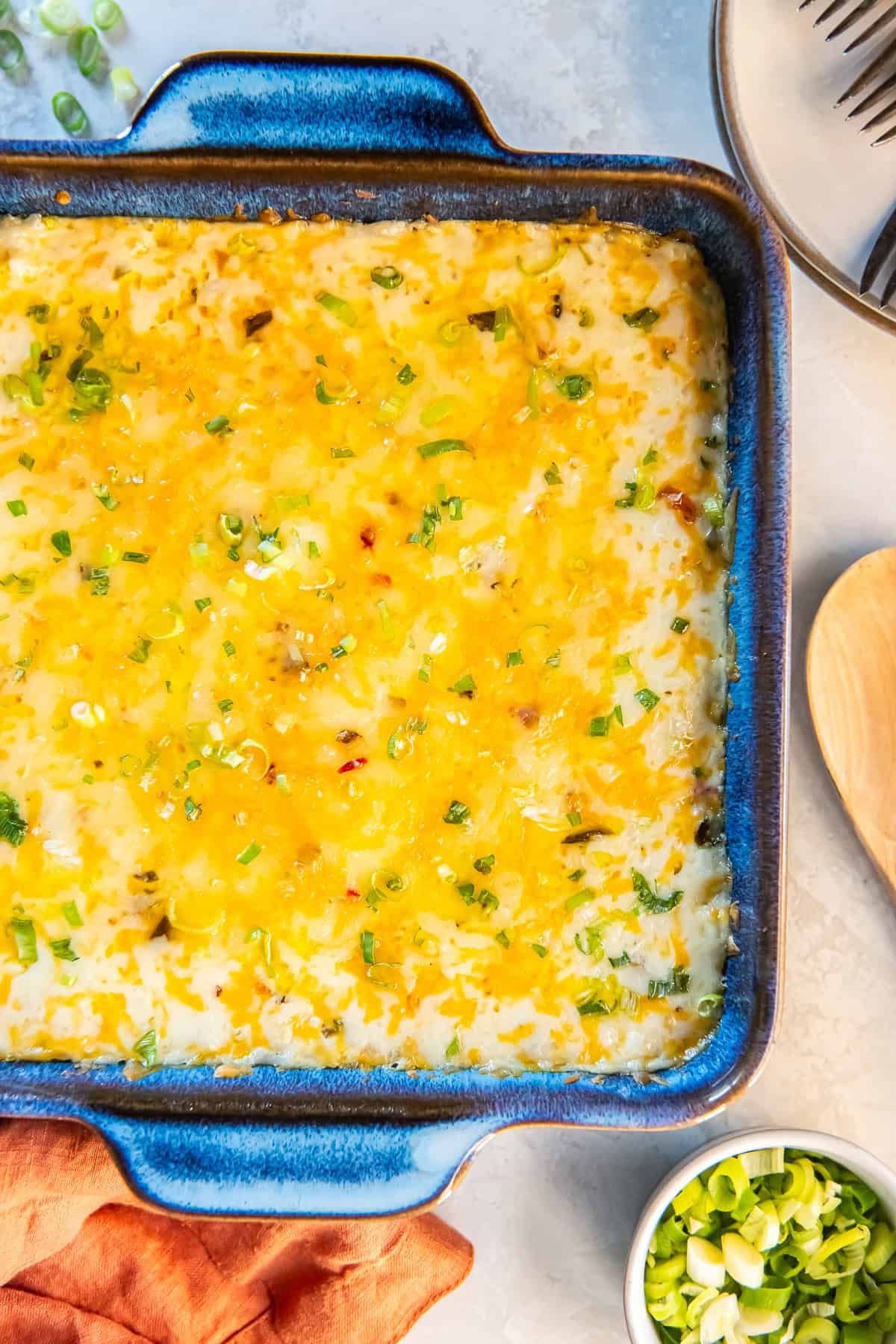 Baked green chile rice casserole in a blue dish, topped with melted cheese and sliced green onions, fresh from the oven.