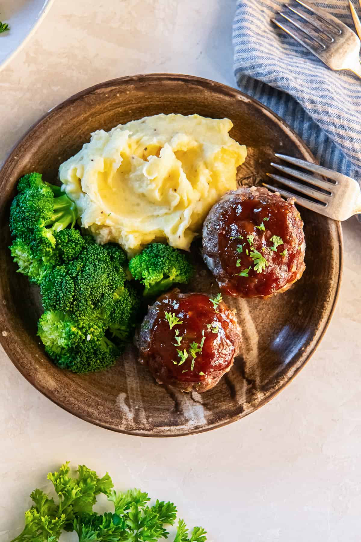 Two meatloaf muffins on a wood plate with mashed potatoes and broccoli.