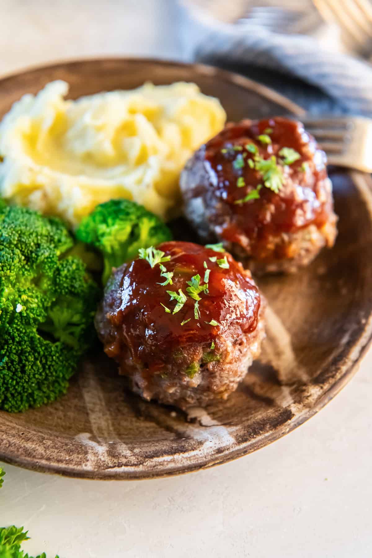 Two meatloaf muffins on a wood plate with mashed potatoes and broccoli.