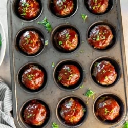 Muffin pan filled with glazed meatloaf muffins surrounded by fresh parsley