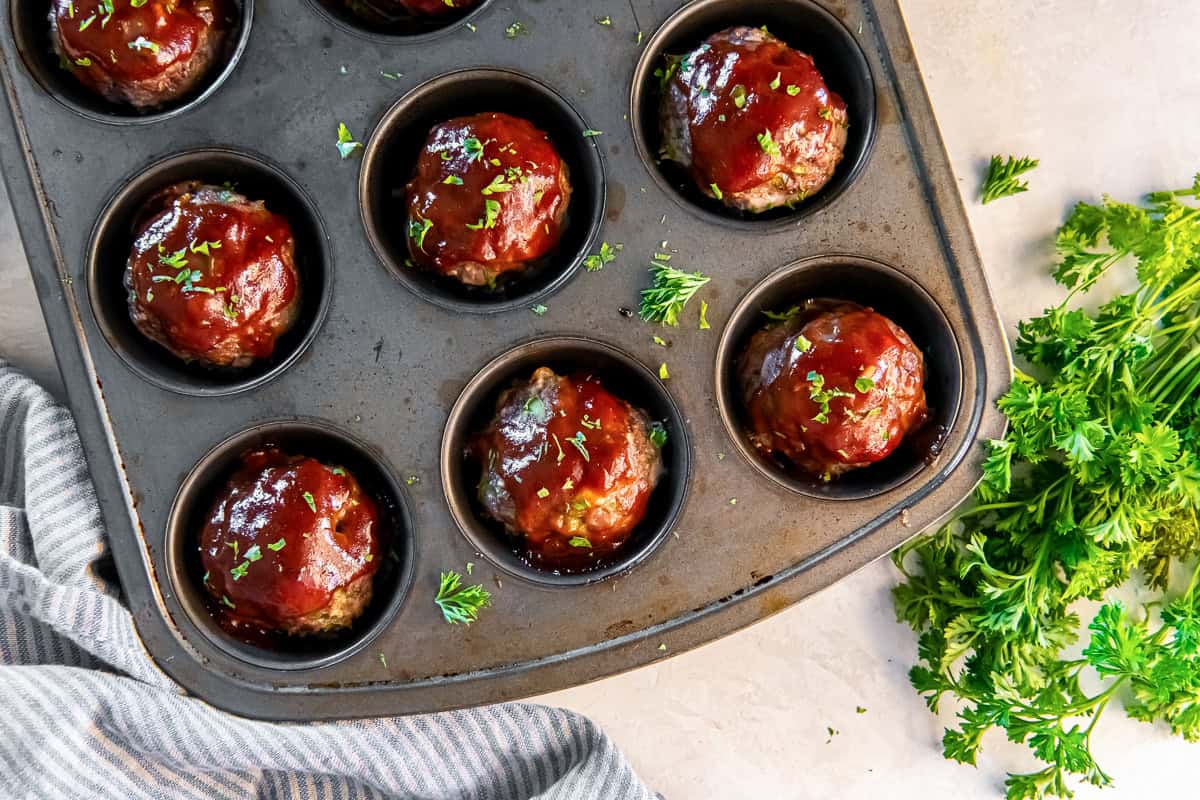 Baked meatloaf muffins in a muffin tin with BBQ glaze and fresh parsley