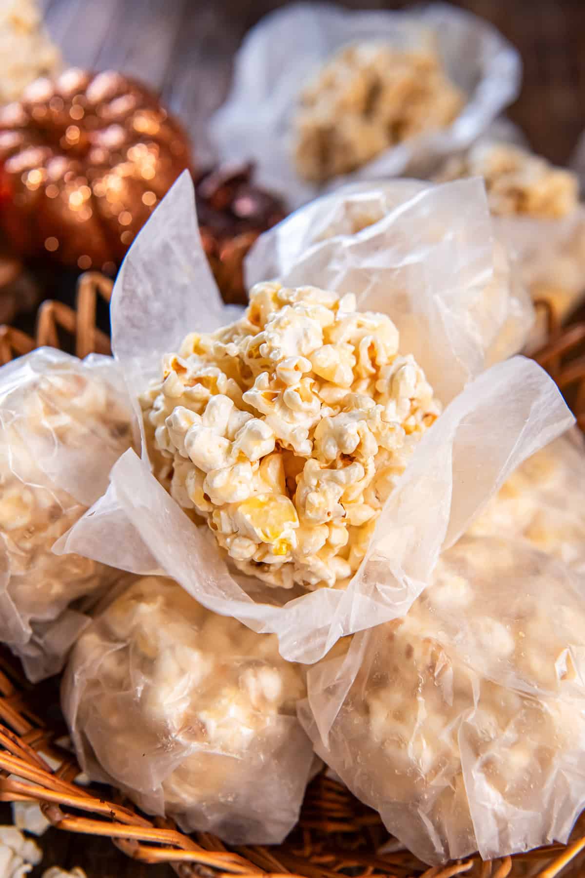 Old-fashioned popcorn ball wrapped in wax paper in a wicker basket, shiny butter-caramel coating