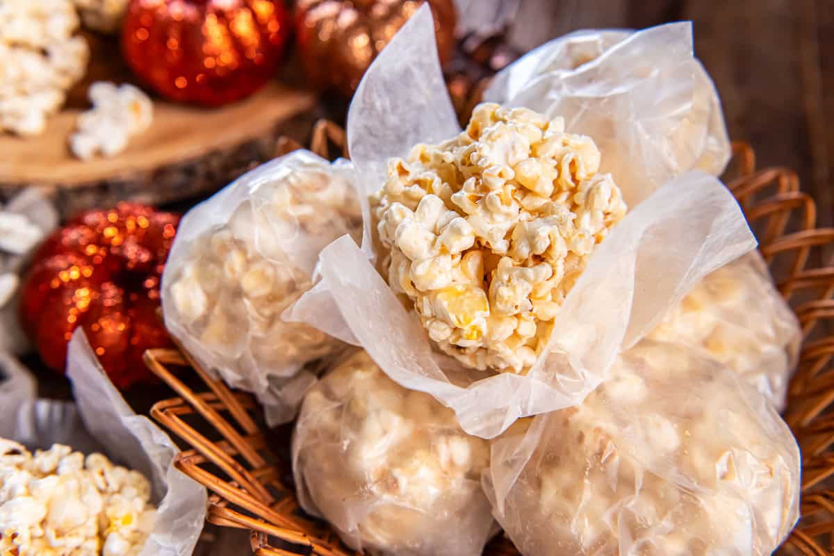 Basket of old-fashioned popcorn balls, most wrapped in wax paper with one unwrapped on top, surrounded by fall decorations.