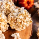 Stack of homemade caramel popcorn balls on a wooden serving board with glittery pumpkins in the background.