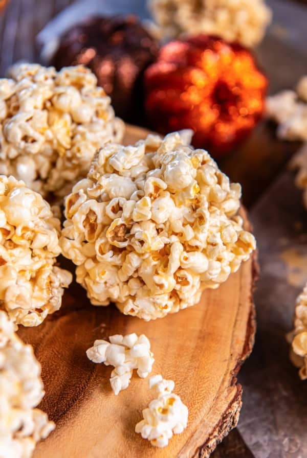 Stack of homemade caramel popcorn balls on a wooden serving board with glittery pumpkins in the background.