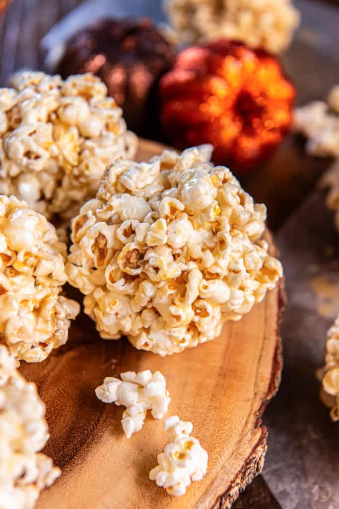 Stack of homemade caramel popcorn balls on a wooden serving board with glittery pumpkins in the background.